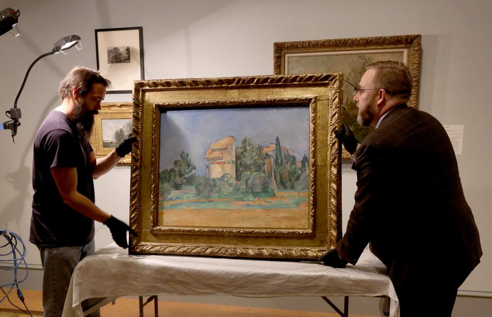 Paul Cezanne's "The Pigeon Tower at Bellevue" is on loan to the Dayton Art Institute from the Cleveland Museum of Art. The DAI's preparator Erich Reith (left) and Per Knutas, chief conservator for the Cleveland Museum of Art, unpacked the painting in October.  LISA POWELL / STAFF