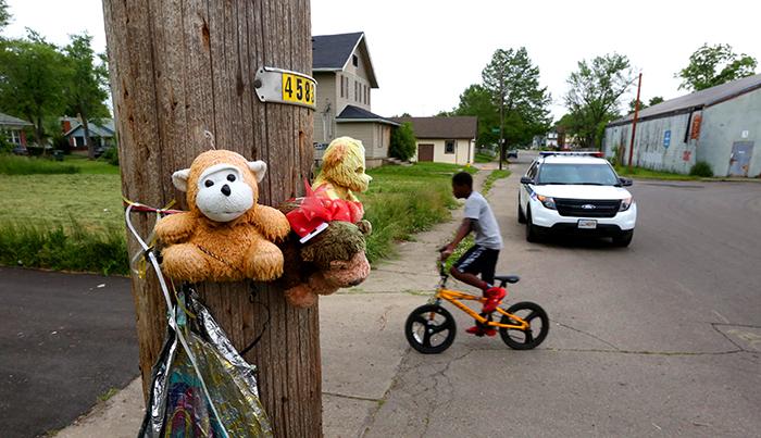 A telephone pole on West Second Street in Dayton is strung with weathered stuffed animals and a deflated balloon marking the spot where a man was found shot to death in October. Children ride their bikes and play basketball across from the memorial. LISA POWELL / STAFF