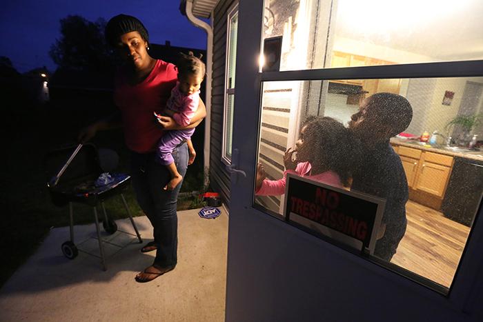 Sherita Brown holds her two-year-old daughter Tayanna as she cooks chicken on a grill. Her children Nailu'j, 5, and Jeron, 8, keep her company.  LISA POWELL / STAFF